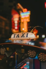 A taxi sign is prominently displayed, surrounded by a blur of colorful neon lights in the background, giving an urban nighttime vibe.