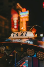 A taxi sign is prominently displayed, surrounded by a blur of colorful neon lights in the background, giving an urban nighttime vibe.