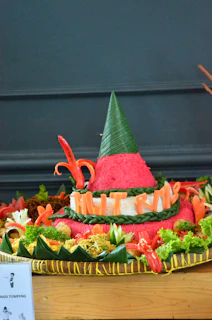 A colorful nasi tumpeng centerpiece surrounded by fresh vegetables and traditional Indonesian garnishes.