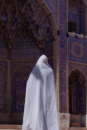 a person wearing a white shawl standing in front of a building
