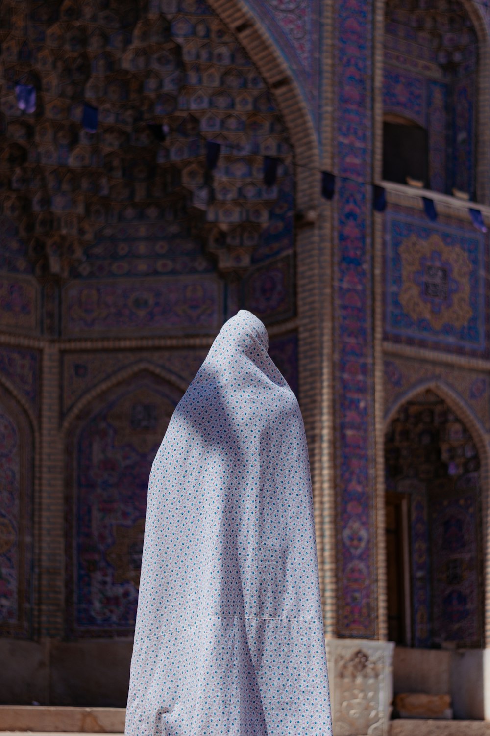 a person wearing a white shawl standing in front of a building