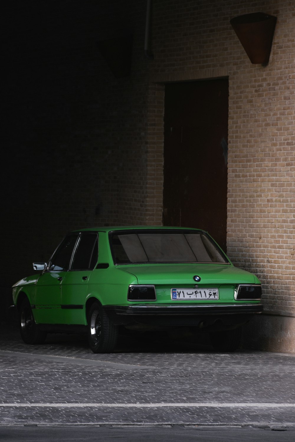 a green car parked next to a brick building