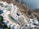 An aerial view of a luxurious coastal resort with multiple swimming pools. The resort features white buildings with terraces and sun loungers, nestled into rocky cliffs overlooking a blue ocean. The landscape is a blend of architectural elegance and natural beauty.