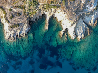 Drone image showing dramatic coastline with turquoise waters and rocky shores under a clear blue sky.