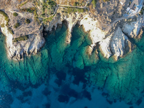 Drone image showing dramatic coastline with turquoise waters and rocky shores under a clear blue sky.