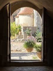 A rustic stone entrance of Cortijo El Maizal surrounded by blooming flowers under a clear blue sky.