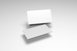 Two blank white business cards are positioned on a light gray surface. One card is slightly elevated above the other, creating a shadow and adding a sense of depth to the image.