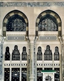 An intricate and ornate architectural facade featuring large arched windows with decorative patterns. The structure is adorned with geometric and floral motifs, displaying detailed craftsmanship in stone and glass. The design combines traditional and artistic elements, emphasized by columns and arches, creating a sense of grandeur.