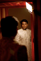 Close-up of a little girl’s hands adjusting the intricate mirror work on her cream sharara set, with soft golden light highlighting the details.