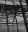 The image features a complex geometric structure composed of crisscrossing metal beams and a perforated metal facade. The design elements create a sense of depth and intricate detail, with light partially filtering through the spaces in between.