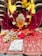 An ornate setup featuring a vibrant and detailed deity idol adorned with an intricately designed silver crown and surrounded by colorful flower garlands. The idol rests on a rich, embroidered red fabric. Additional elements include floral arrangements and a symbolic marking featuring feet impressions on a silver plaque.