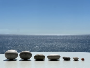 A collection of blue and white natural stone bracelets arranged on a rocky shore with the ocean in the background.