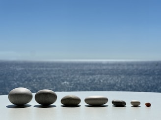 A collection of blue and white natural stone bracelets arranged on a rocky shore with the ocean in the background.