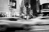 Black and white photo of a bustling city crosswalk with blurred motion.