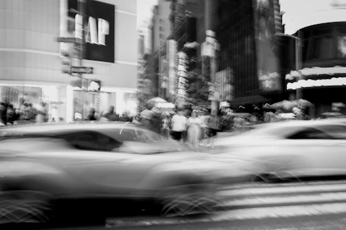 Black and white photo of a bustling city crosswalk with blurred motion.