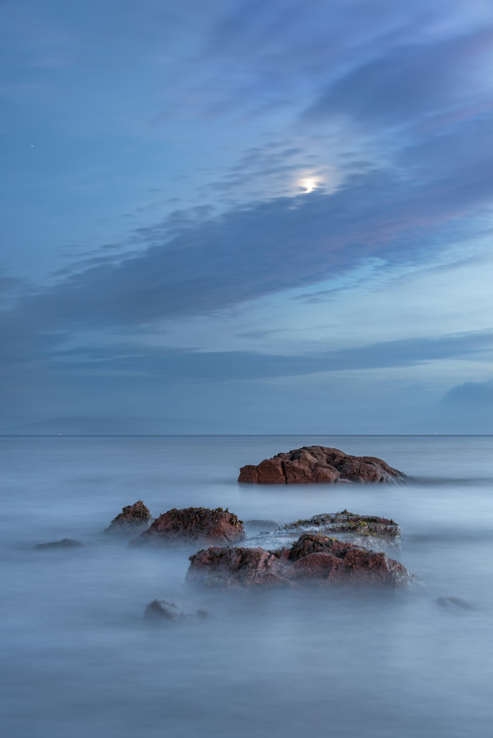 a long exposure photo of the moon rising over the ocean