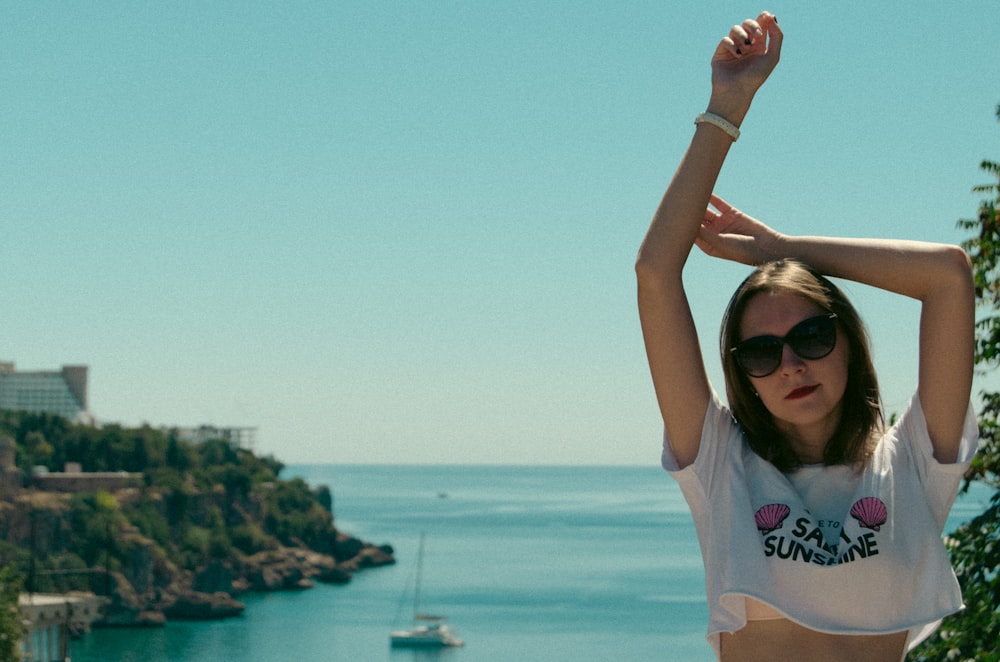 a woman in a white shirt and sunglasses standing in front of a body of water