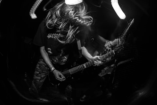 A dynamic black-and-white photo of Headrush performing live, with red stage lights casting bold shadows.
