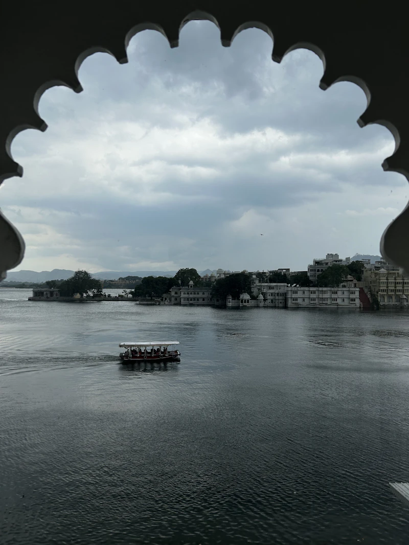 A boat on Lake Pichola in Udaipur seen through a scalloped palace arch under monsoon clouds