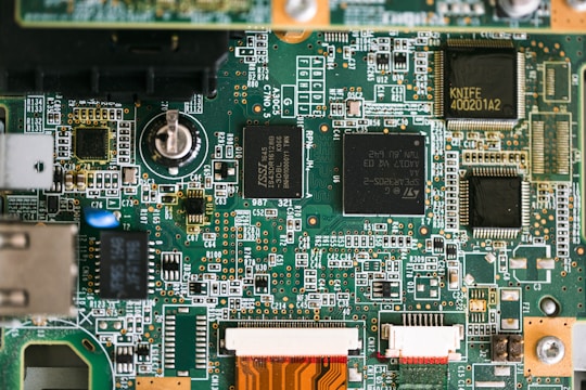 A detailed view of a printed circuit board (PCB) featuring various electronic components. Several integrated circuits or chips are prominently placed on the green board, surrounded by a network of copper traces and connections. Smaller components like resistors, capacitors, and connectors are also visible, adding to the intricacy of the design.