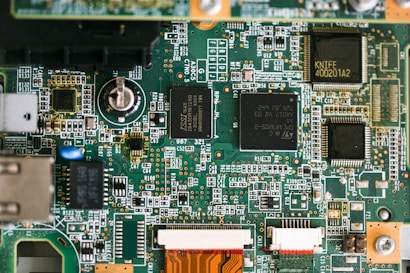 A detailed view of a printed circuit board (PCB) featuring various electronic components. Several integrated circuits or chips are prominently placed on the green board, surrounded by a network of copper traces and connections. Smaller components like resistors, capacitors, and connectors are also visible, adding to the intricacy of the design.
