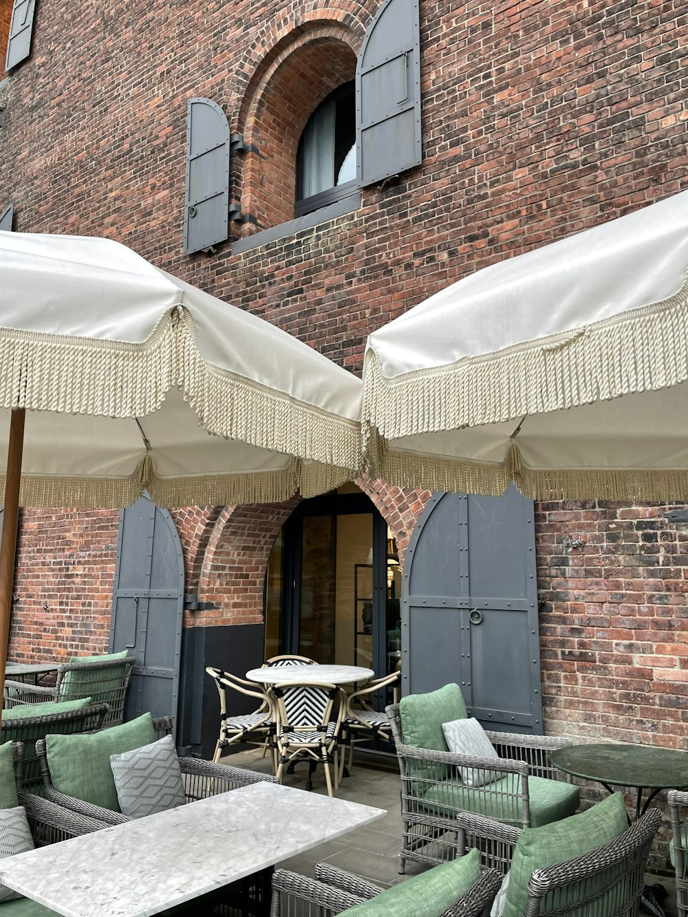 tables and chairs with umbrellas in front of a brick building