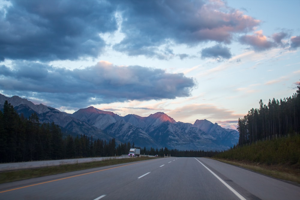 a truck driving down a road with mountains in the background