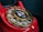 A close-up of a vintage red rotary telephone with a gold dial that has numbers arranged in a circular fashion. The central part of the dial features a sticker with the words 'Wait for dial tone' and an image of a telephone handset.