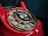 A close-up of a vintage red rotary telephone with a gold dial that has numbers arranged in a circular fashion. The central part of the dial features a sticker with the words 'Wait for dial tone' and an image of a telephone handset.
