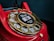 A close-up of a vintage red rotary telephone with a gold dial that has numbers arranged in a circular fashion. The central part of the dial features a sticker with the words 'Wait for dial tone' and an image of a telephone handset.