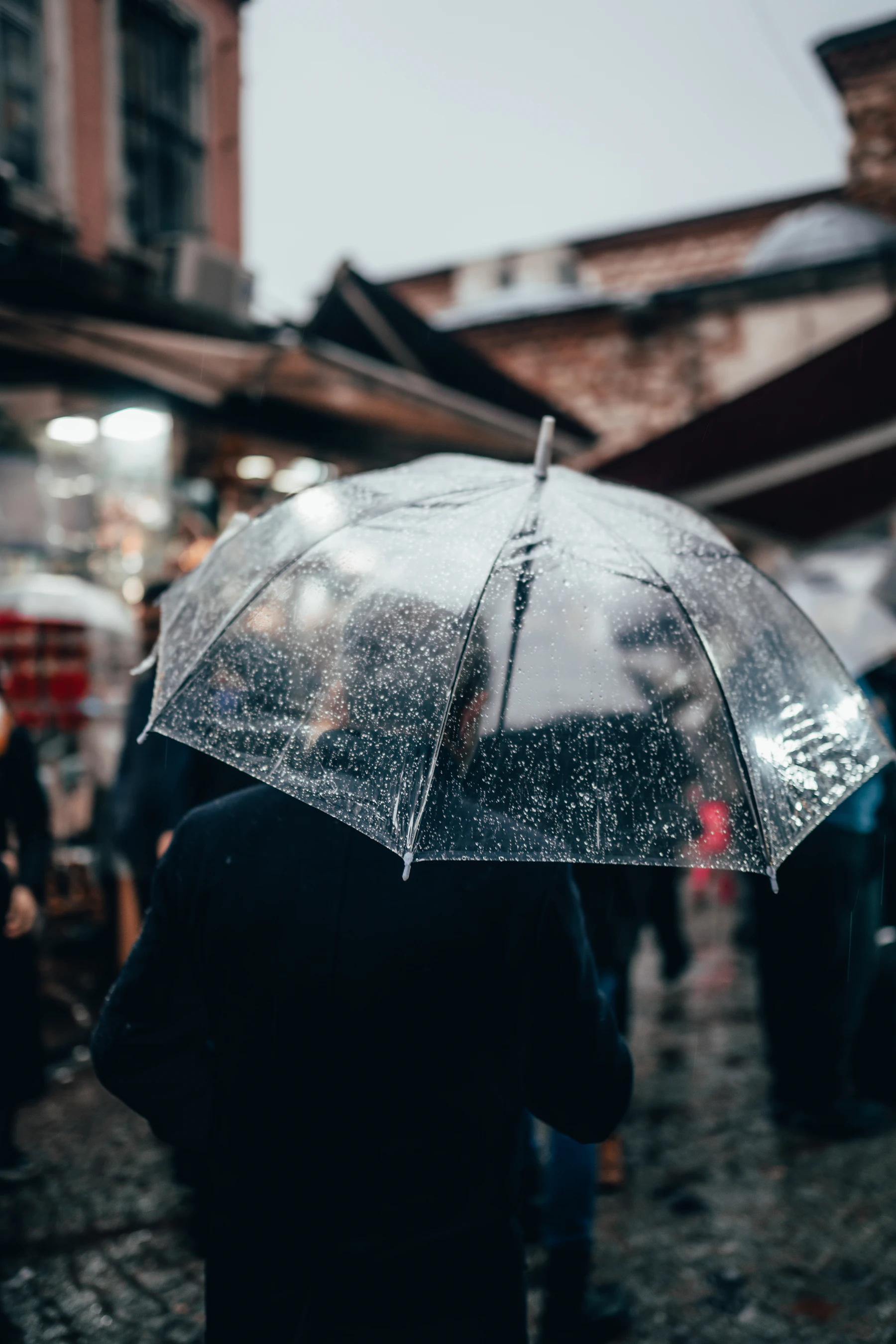 A traveller walks through a wet city street beneath a clear umbrella.