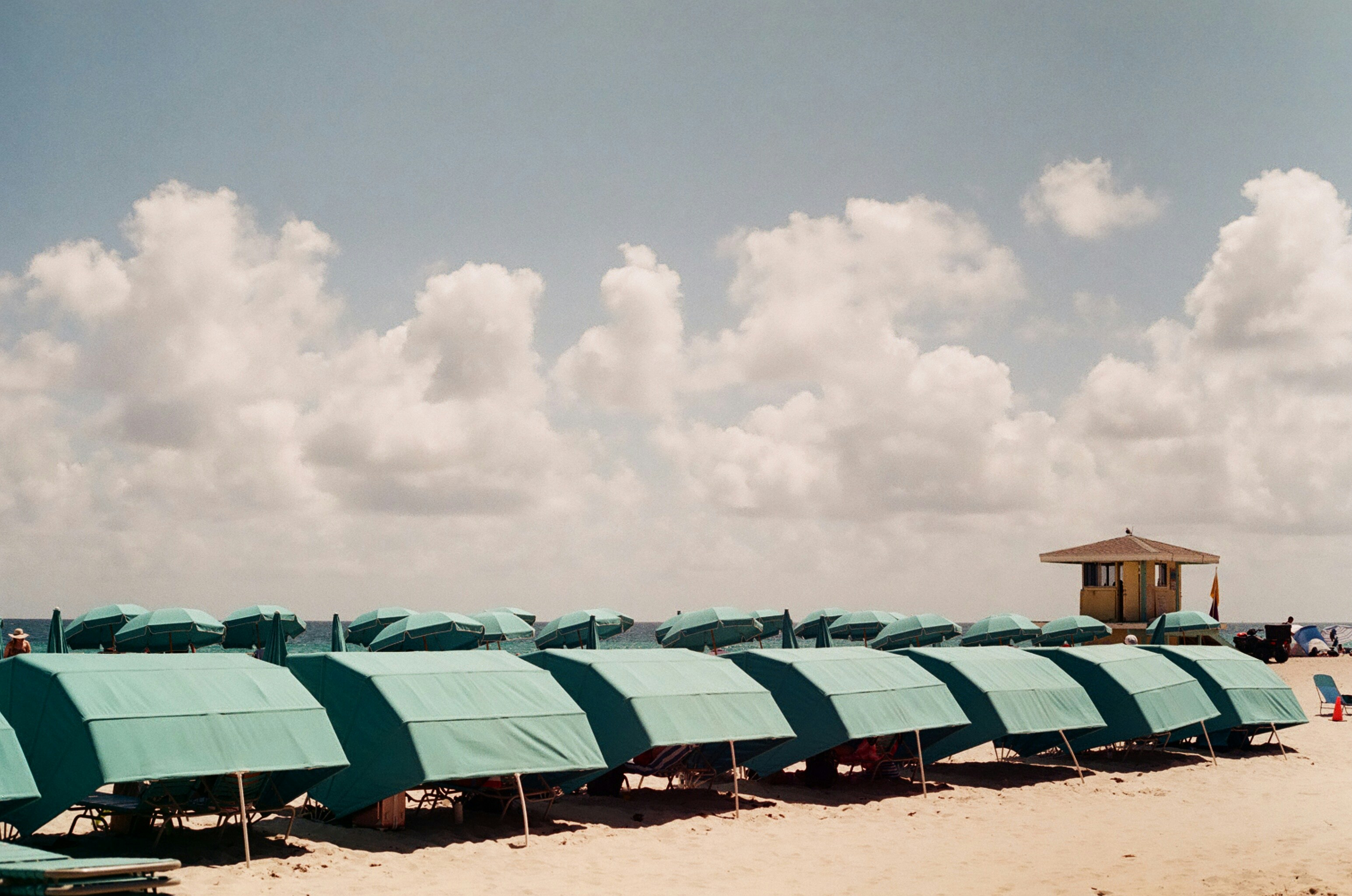 a row of green beach chairs sitting on top of a sandy beach