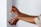 A person is applying an essential oil roller to their forearm. The bottle is amber-colored and has a label. The person is holding the cap in their other hand, and they are wearing rings.