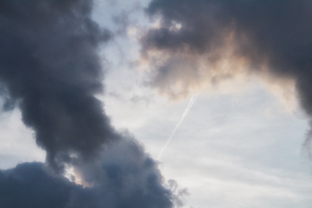 a plane flying through a cloudy sky with contrails