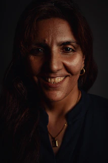 A smiling customer wearing a unique handcrafted necklace under soft, moody lighting.