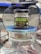 A jar of organic Black Forest honey sits on top of a large glass container with a blue lid. The jar has a black lid and features bold green and yellow labels with text in English and Arabic.