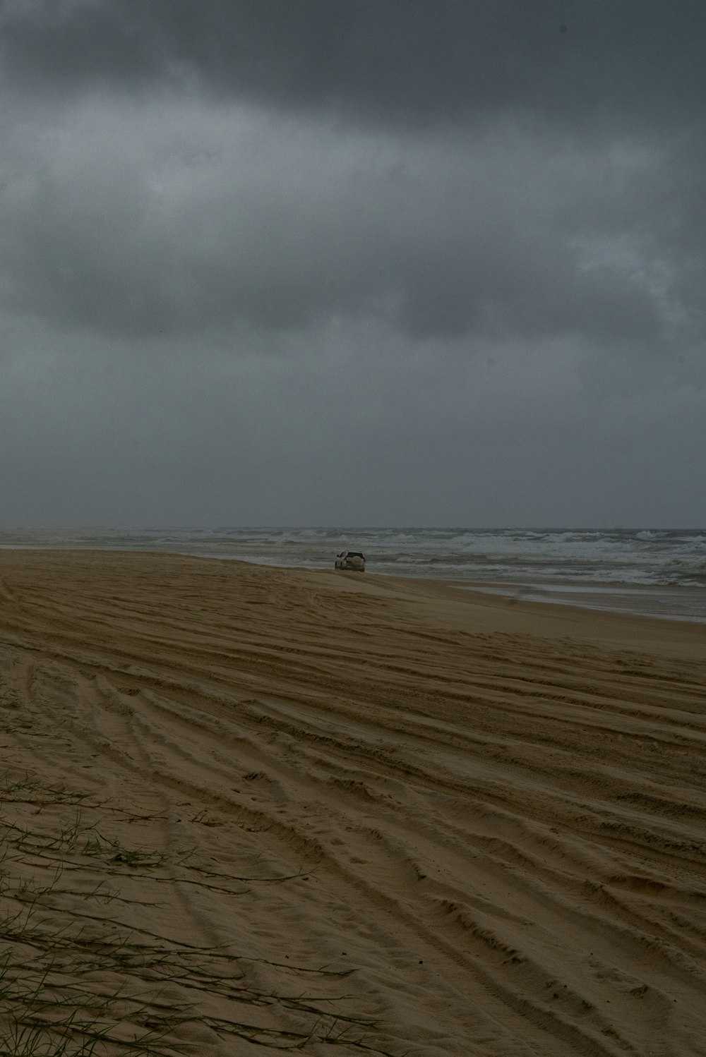 a truck driving down a sandy beach under a cloudy sky