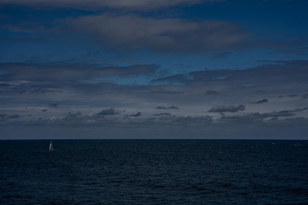 a sailboat in the middle of the ocean under a cloudy sky