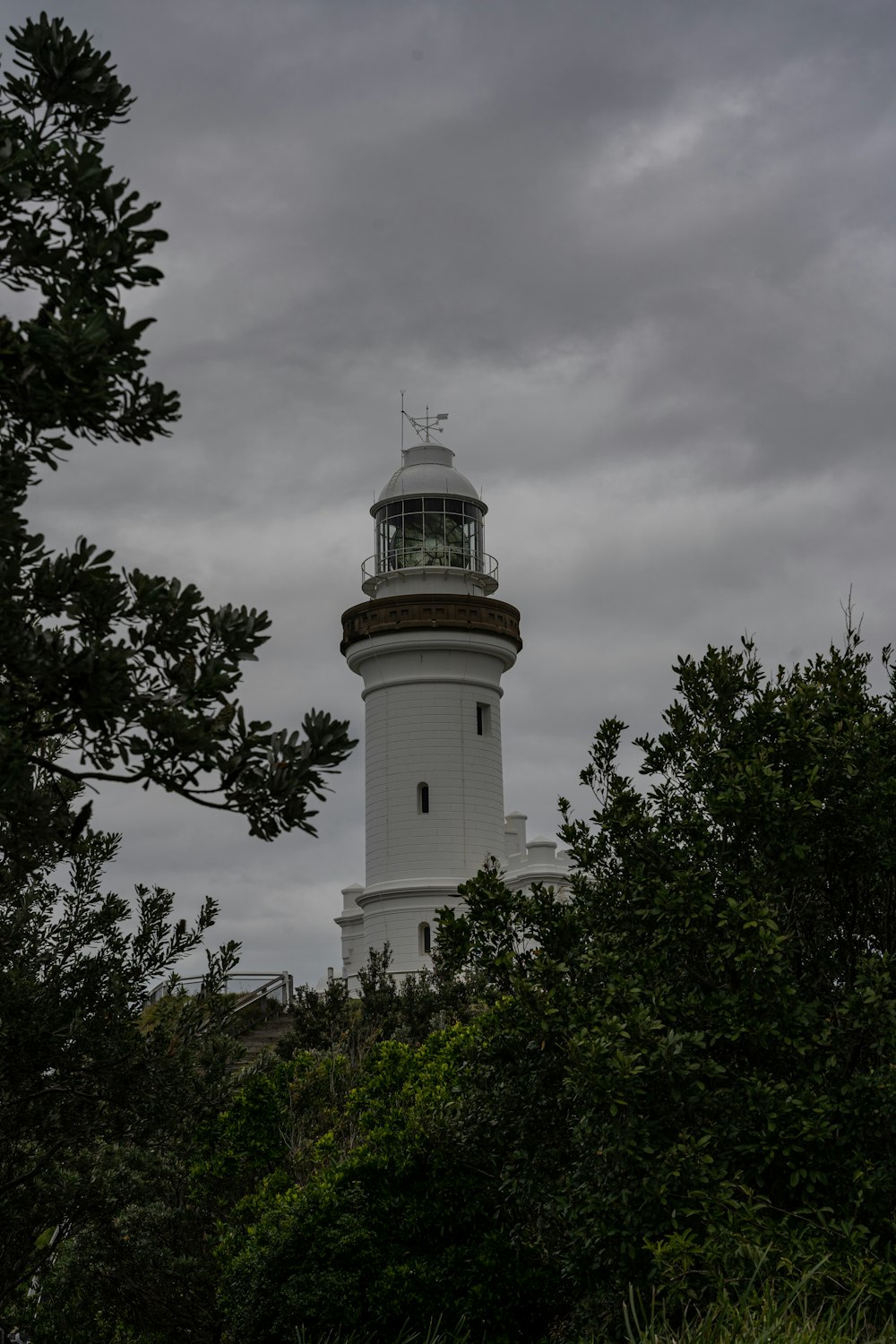 a white lighthouse surrounded by trees under a cloudy sky
