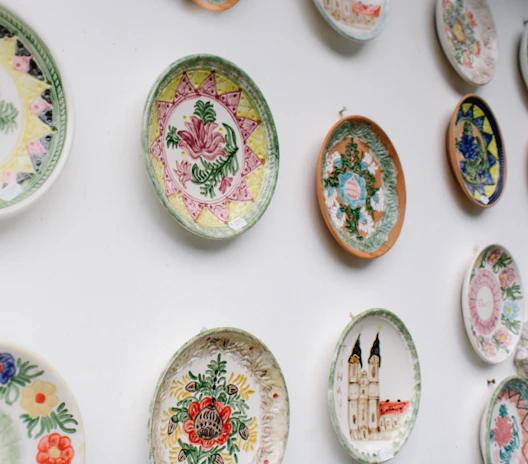 A collection of colorful ceramic plates with hand-painted details, arranged in an artful pattern on a white wall.