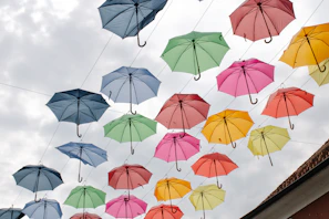 A whimsical umbrella with colorful panels twirling above café tables on a light rainy afternoon.