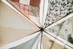 Various fabric panels with intricate patterns and earthy tones are stretched out and attached to wooden poles, creating a visually appealing canopy. The fabrics feature geometric and floral designs, adding an artistic flair.
