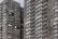 A high-rise residential building with dark gray brick facade and numerous windows. The structure features repeating patterns of balconies and windows, providing a uniform appearance. One person can be seen on a balcony, offering a sense of scale and activity.