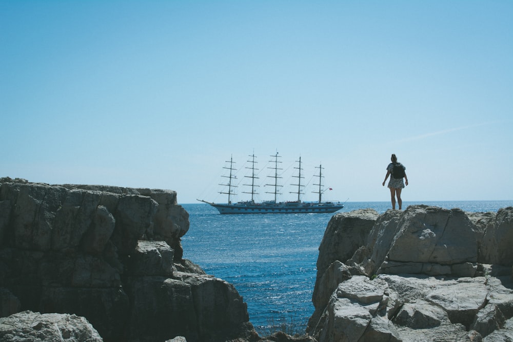 a person standing on a rock looking at a ship