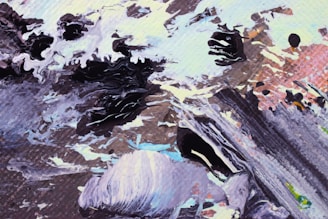 An abstract artwork featuring dynamic swirling patterns of black, white, and earth tones. Layers of paint create texture and movement, suggesting natural elements like rocks and water. The colors blend seamlessly into each other, creating a sense of flow.