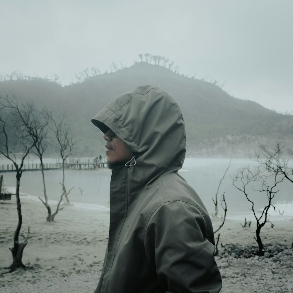 a man in a hooded jacket standing in front of a body of water