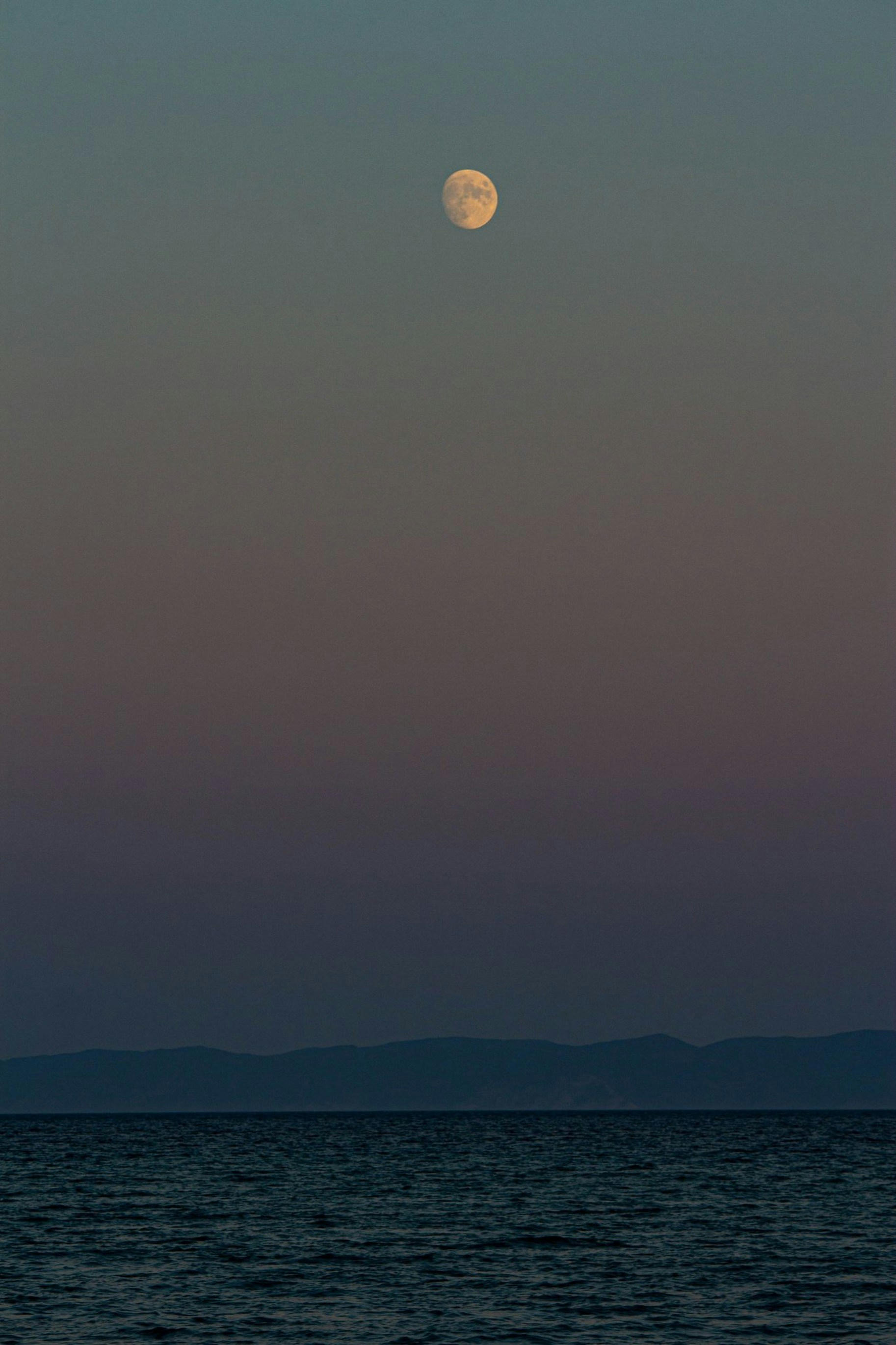 a-full-moon-rising-over-the-ocean-with-mountains-in-the-background-byVmN2h-bsY