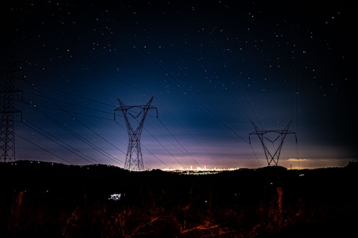 Nighttime aerial shot of Assam’s illuminated power stations and distribution lines.