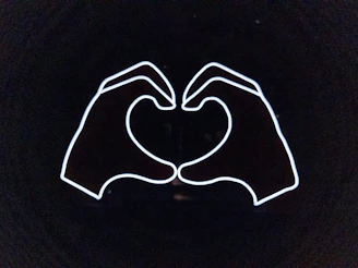 A warm illustration of two hands reaching out with a pink heart glowing between them on a clean white background.