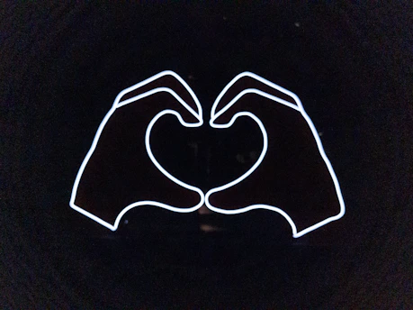 A close-up of two hands gently holding a glowing heart symbol, set against a deep blue background.
